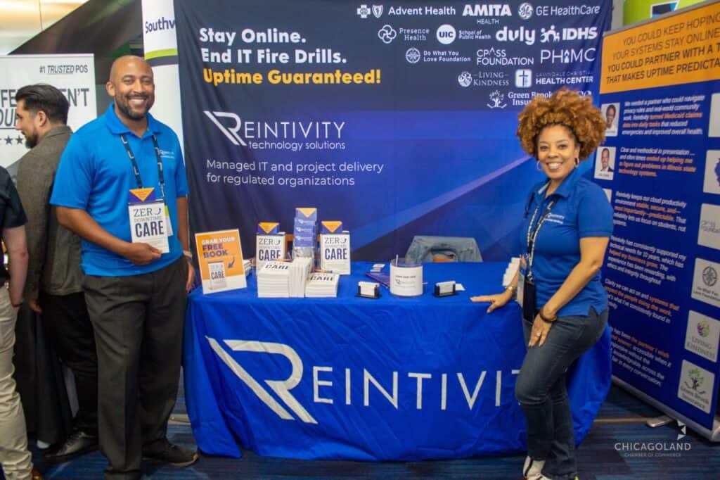 Reintivity team members at Booth 52 during The Exchange 2026, holding and displaying copies of &ldquo;Zero-Downtime Care,&rdquo; engaging attendees on reducing IT fire drills, improving system reliability, and creating more predictable operations.