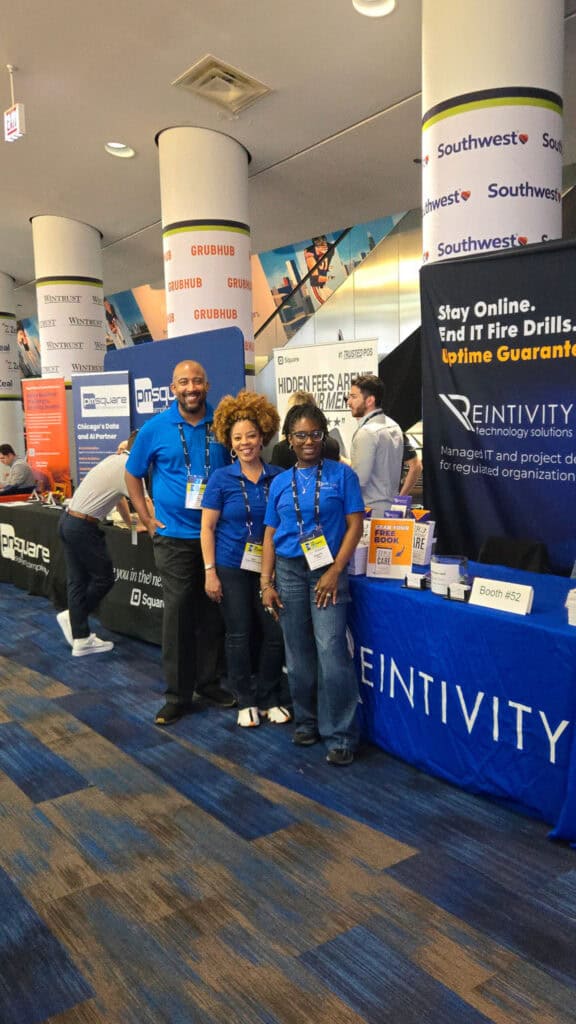 Reintivity team members standing at Booth 52 during The Exchange 2026 by Chicagoland Chamber of Commerce held at Soldier Field, speaking with attendees about reducing IT fire drills, improving security, and streamlining workflows for more stable and predictable operations.